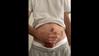 a skinny guy in white briefs, gray sweatpants, a white T-shirt jerks off his dick in his room