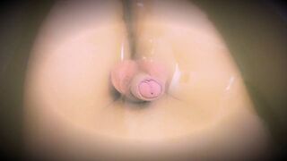 A young, thin, and slender guy is bathing in the tub, his penis dangling in the water